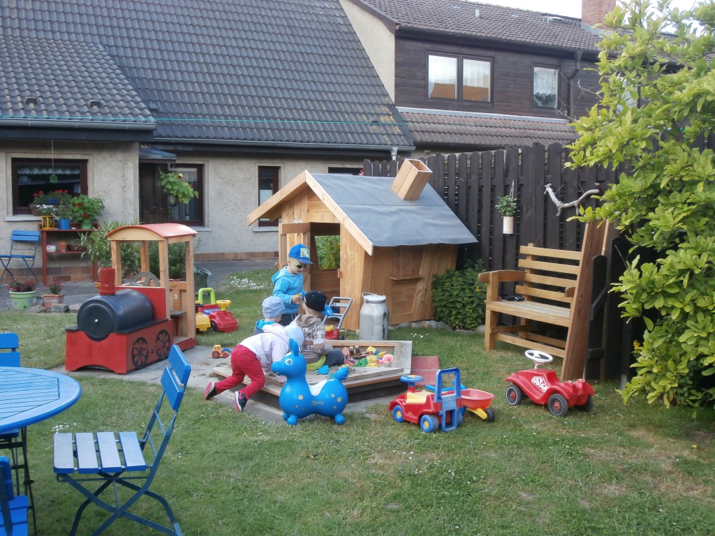 Blick in den Garten mit Spielgeräten und Häuschen.